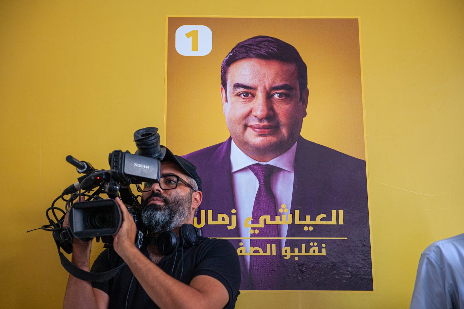 A cameraman films a press conference held by Abdessatar Messaoudi, attorney of Tunisian presidential candidate Ayachi Zammel, seen on the poster on the wall, after Zammel was sentenced to prison on fraud charges that Messaoudi decried as politically motivated, in Tunis, Monday, Sept. 16, 2024 (AP Photo/Ons Abid)