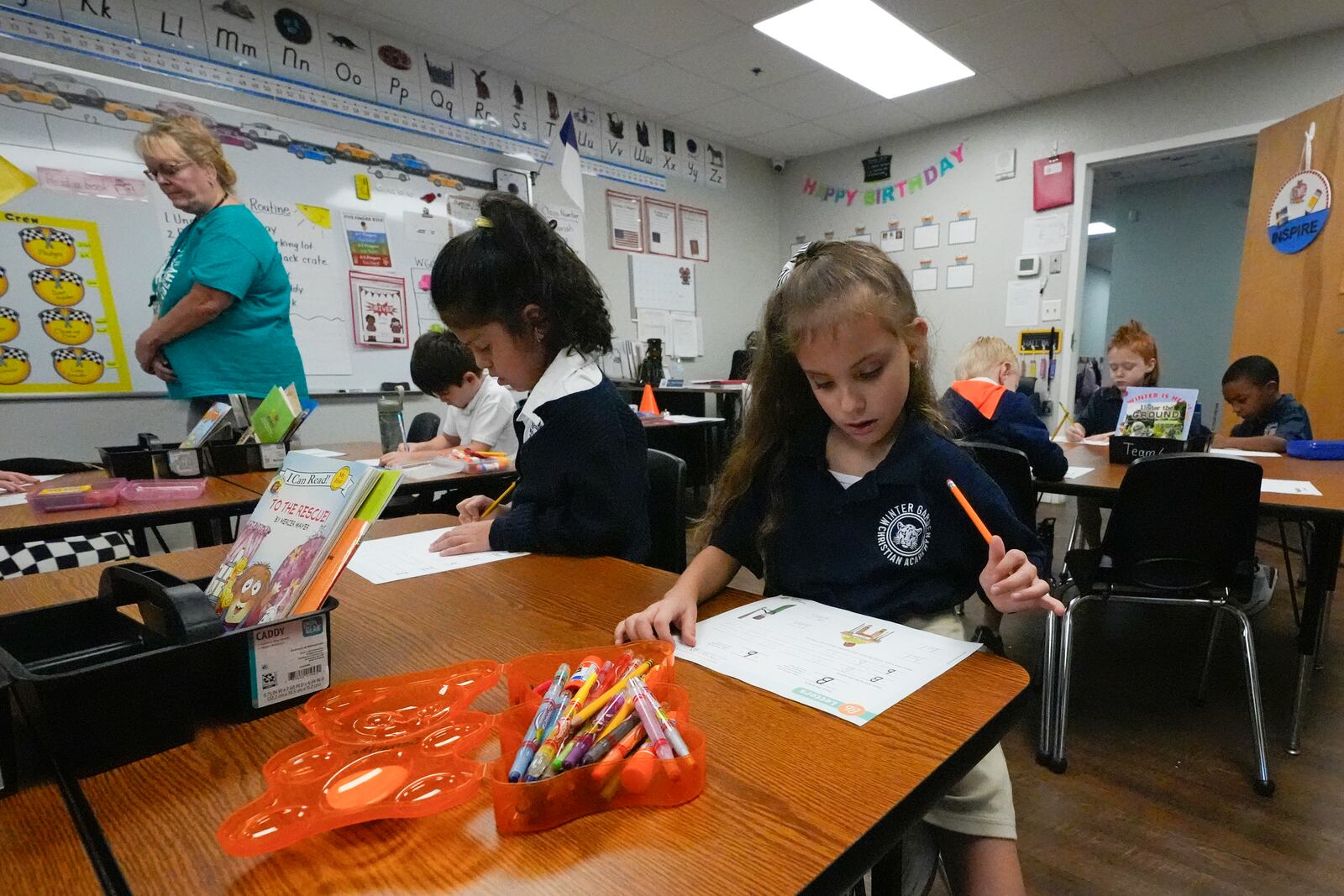 First grade teacher Sharon Parsons, back left, checks on students working in the classroom at the Winter Garden Christian Academy Thursday, Aug. 29, 2024, in Winter Garden, Fla. (AP Photo/John Raoux)