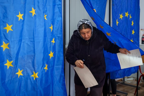 A woman exits a voting cabin with European Union flags as curtains before casting her vote in the country's parliamentary elections, in Baleni, Romania, Sunday, Dec. 1, 2024. (AP Photo/Vadim Ghirda)