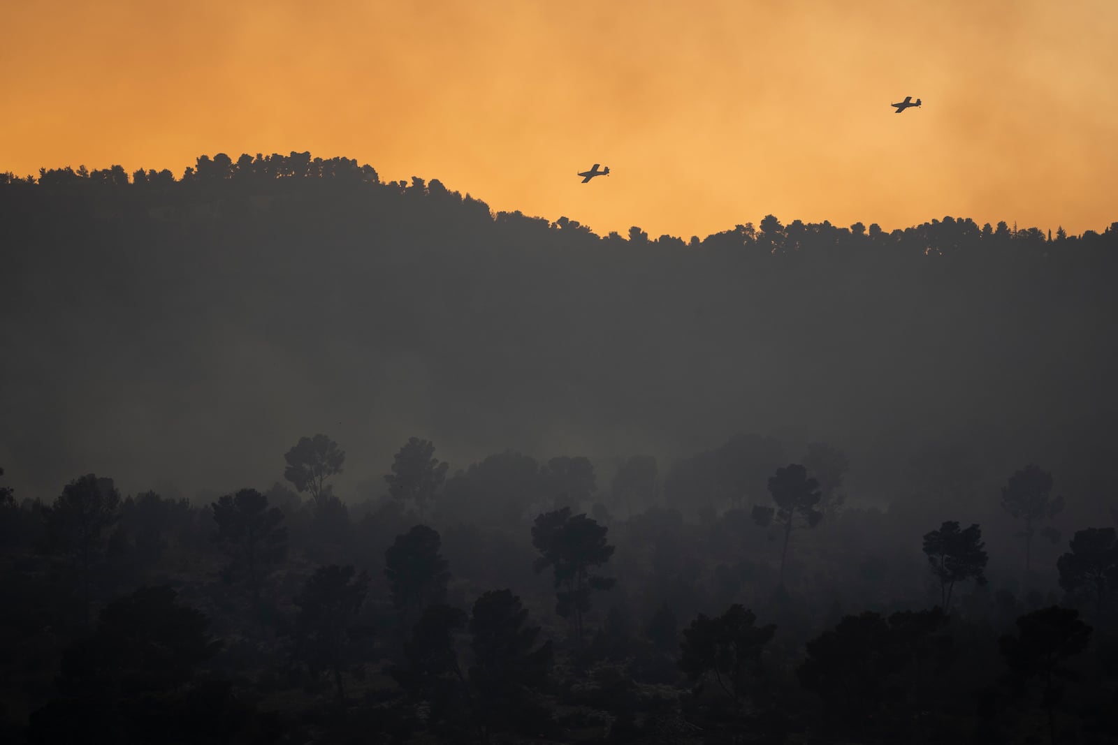 Israeli firefighting planes fly above smoke from a fire after a rocket, fired from Lebanon, hit an area near the town of Hatzor Haglilit, northern Israel, Wednesday, Oct. 9, 2024. (AP Photo/Leo Correa)