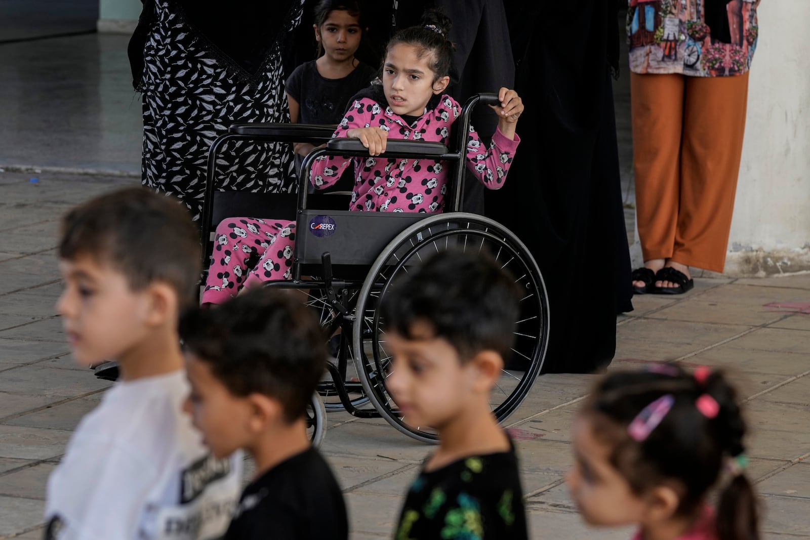 Zahraa on a wheel chair looks on as volunteers of the Russian Cultural Center entertain displaced children at a school in Beirut, Lebanon, Thursday, Oct. 3, 2024, after fleeing the Israeli airstrikes in the south. (AP Photo/Bilal Hussein)