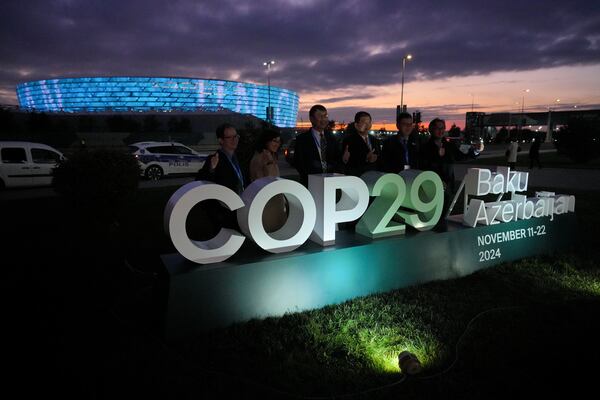 People pose for a photo with the Baku Olympic Stadium in the background at the COP29 U.N. Climate Summit, Thursday, Nov. 14, 2024, in Baku, Azerbaijan. (AP Photo/Peter Dejong)