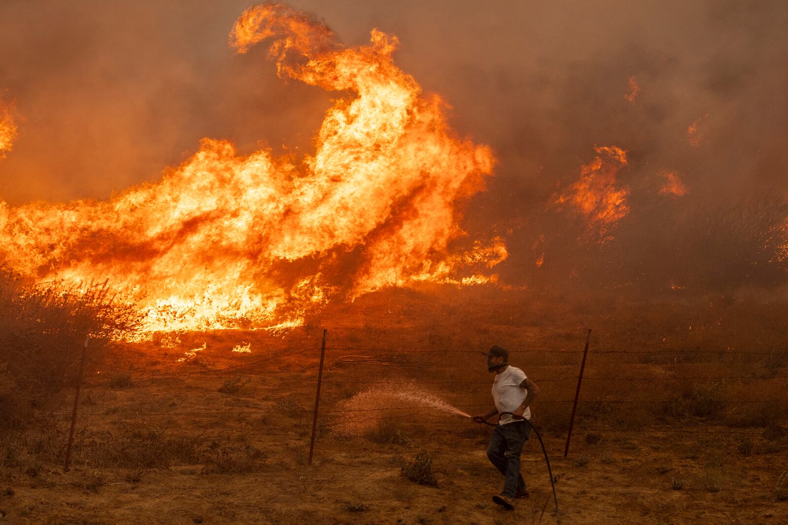 Jaime Hernandez sprays water to defend his home while battling approaching flames from the Mountain Fire near Moorpark, Calif., on Thursday, Nov. 7, 2024. Hernandez has been staying behind to fight multiple wildfires since 1988. (Stephen Lam/San Francisco Chronicle via AP)