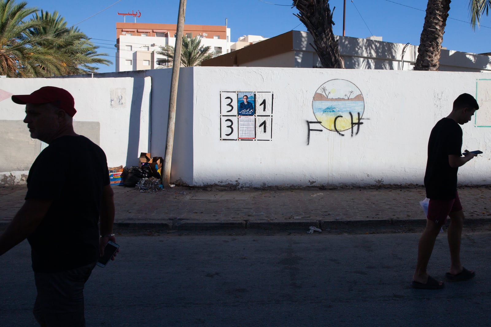 People walk past a wall with electoral banners in Sfax, Tunisia, Sunday, Sept. 15, 2024, ahead of the upcoming presidential elections. (AP Photo/Ons Abid)