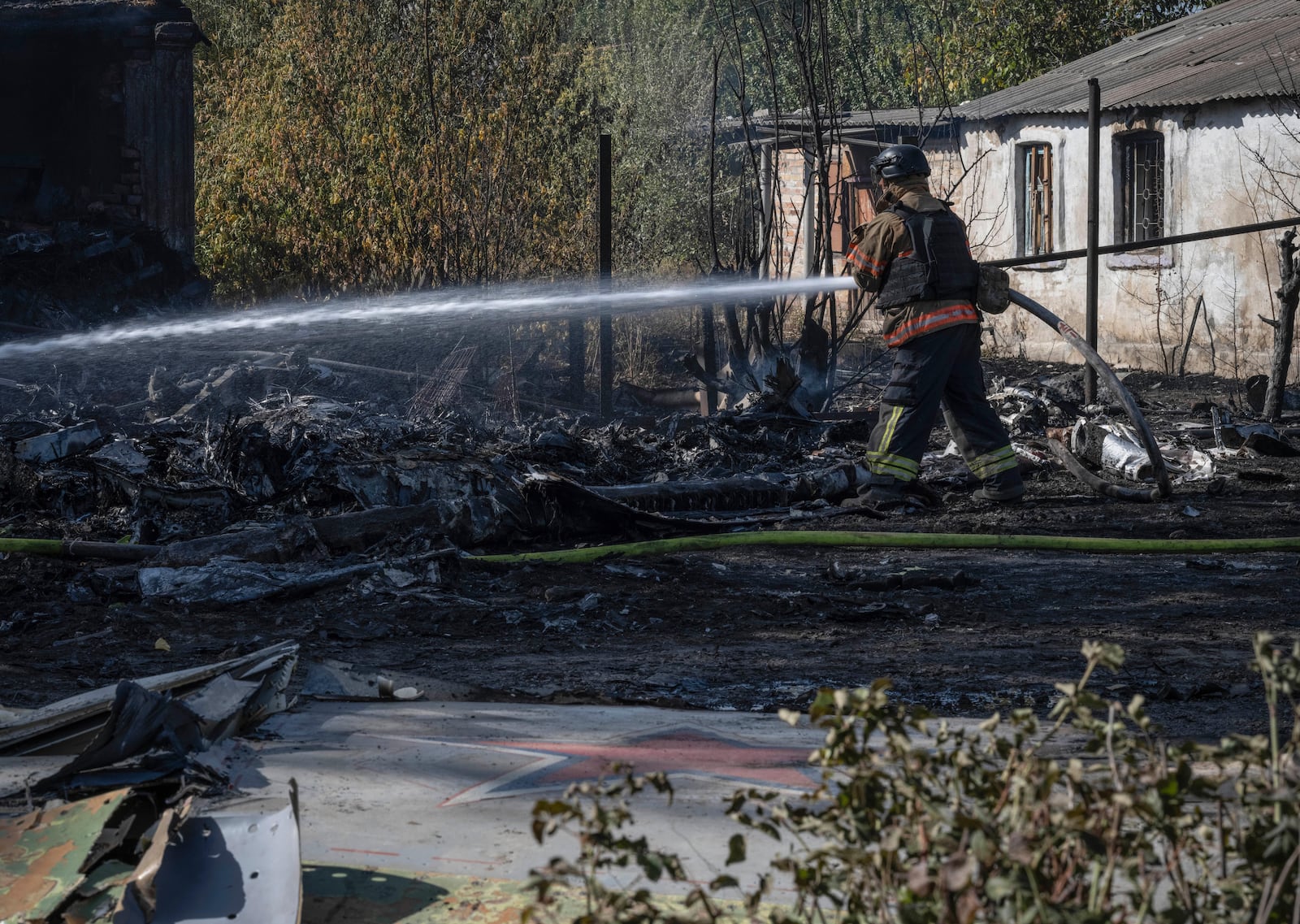 A firefighter puts out the fire after fragments of the downed Russian military plane damaged private houses, on the outskirts of Kostyantynivka, a near-front line city in the Donetsk region, Ukraine, Saturday, Oct. 5, 2024. (Iryna Rybakova via AP)