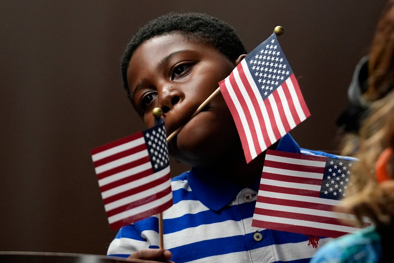 A young boy watches as people take the oath to become American citizens during a naturalization ceremony at the high school attended by former President Jimmy Carter Tuesday, Oct. 1, 2024, in Plains, Ga. (AP Photo/John Bazemore)