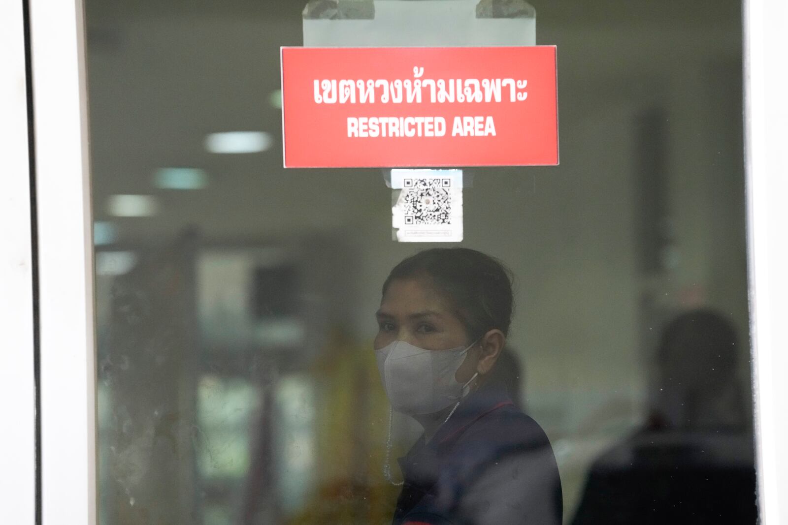 A forensic officer stands behind the forensic department at a police hospital in Bangkok, Thailand, Wednesday, Oct. 2, 2024, as family members of victims visit there after a bus carrying students and teachers caught a fire Tuesday. (AP Photo/Sakchai Lalit)