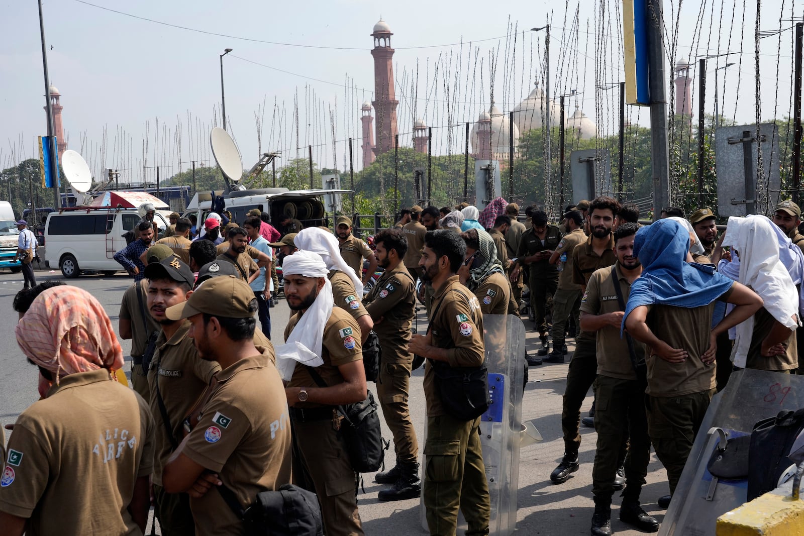 Police officers stand guard next to shipping containers set up by authorities to block a road leading to important government buildings in an attempt to prevent supporters of imprisoned former Prime Minister Imran Khan from holding a rally in Lahore, Pakistan, Saturday, Oct. 5, 2024. (AP Photo/K.M. Chaudary)