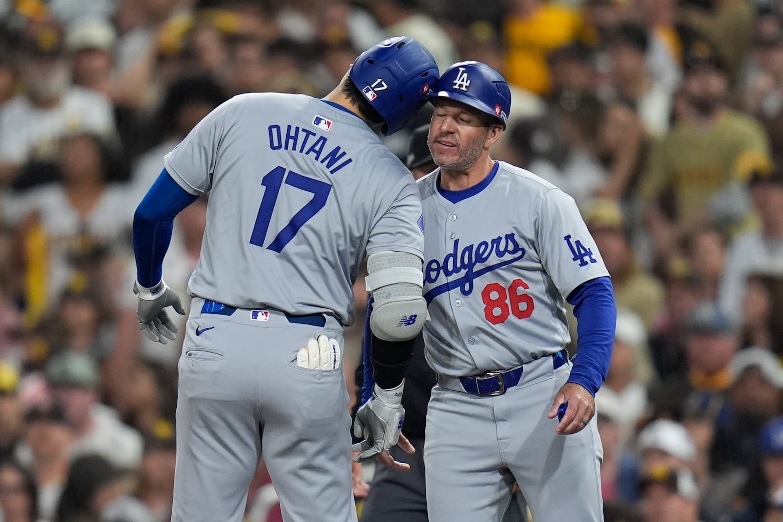 Los Angeles Dodgers' Shohei Ohtani celebrates with first base coach Clayton McCullough after an RBI single during the second inning in Game 4 of a baseball NL Division Series against the San Diego Padres, Wednesday, Oct. 9, 2024, in San Diego. (AP Photo/Gregory Bull)