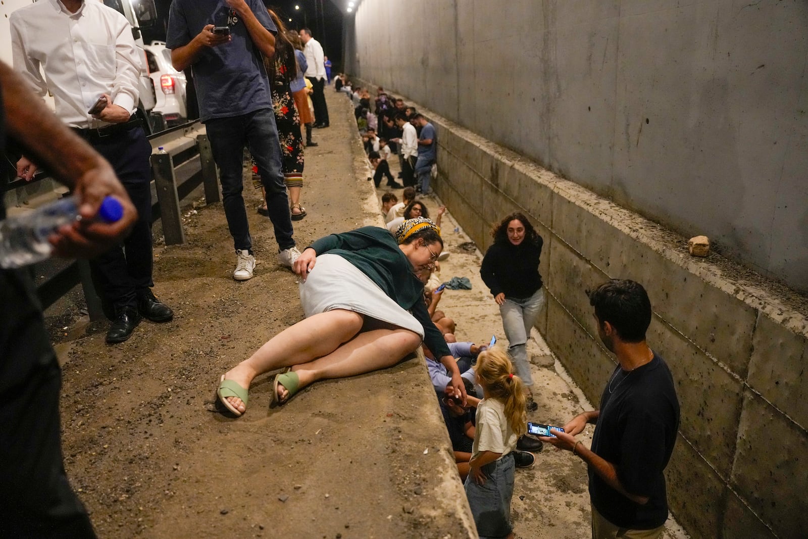 People take cover on the side of a road as a siren sounds a warning of incoming missiles on a freeway in Shoresh, Israel Tuesday, Oct. 1, 2024. (AP Photo/Ohad Zwigenberg)