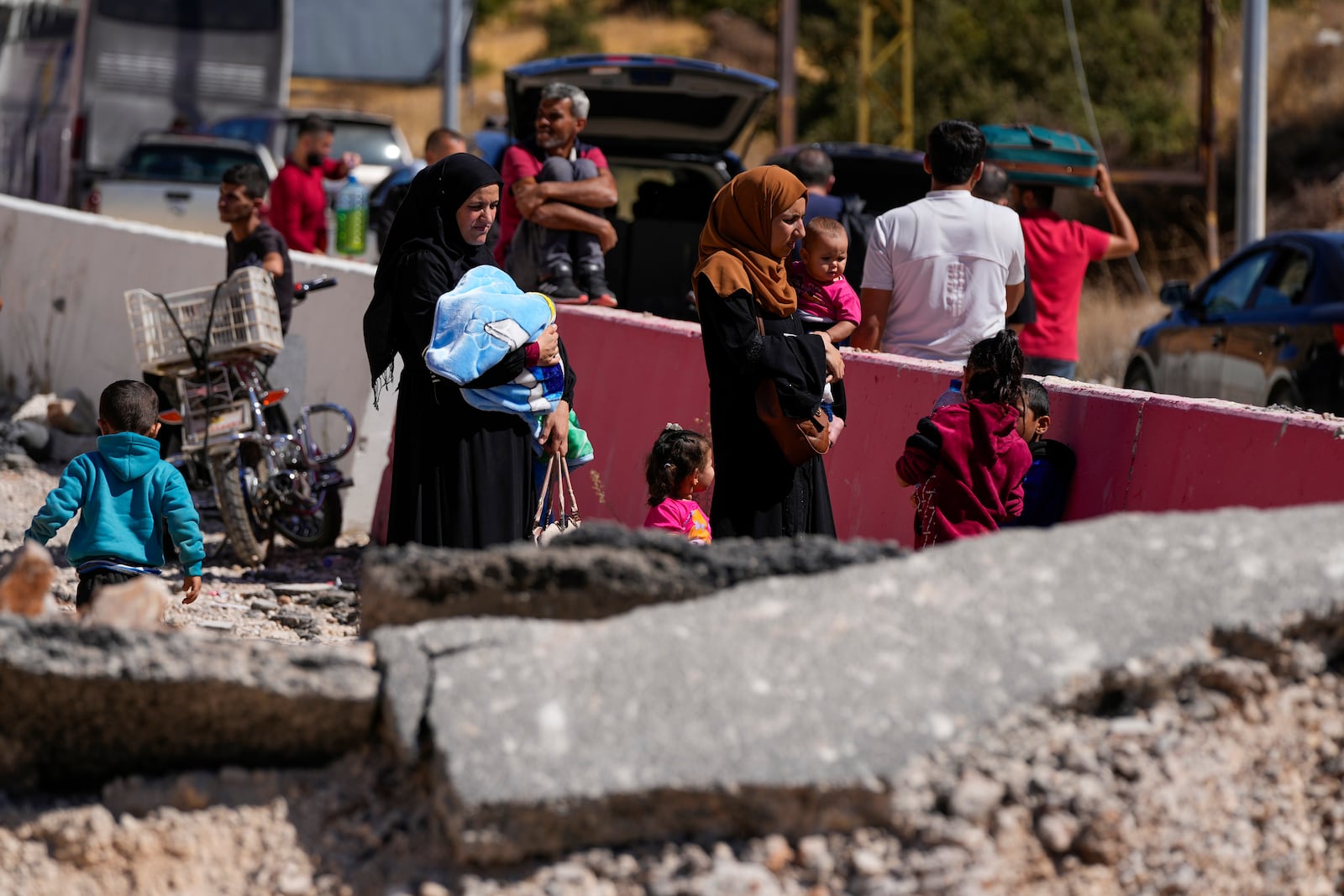 People carry their luggage as they cross into Syria on foot, through a crater caused by Israeli airstrikes aiming to block Beirut-Damascus highway at the Masnaa crossing, in the eastern Bekaa Valley, Lebanon, Saturday, Oct. 5, 2024. (AP Photo/Hassan Ammar)