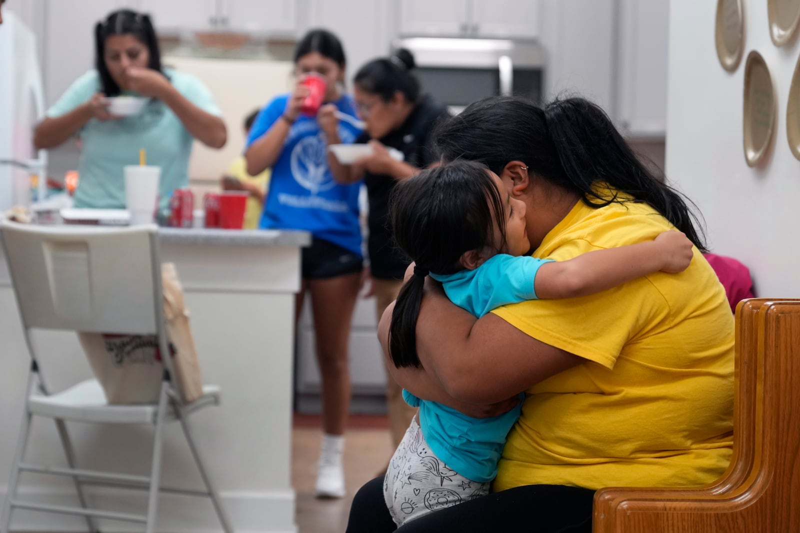 Alexandra Reynoso, right, hugs her little sister, Sofia Reynosa, 5, as others grab a bite to eat in the kitchen of St. Michael the Archangel Catholic church in the aftermath of Hurricane Helene Friday, Oct. 4, 2024, in Erwin, Tenn. (AP Photo/Jeff Roberson)