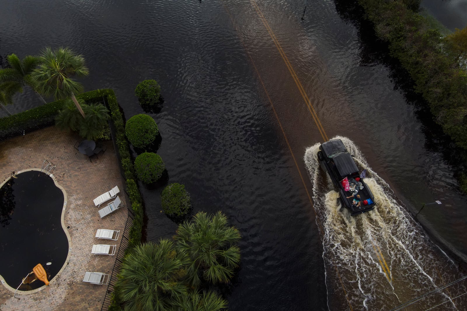 People ride in the back of a pickup avoiding floodwaters in the Tarpon Woods neighborhood of Palm Harbor, Fla., following Hurricane Milton, Friday, Oct. 11, 2024. (AP Photo/Julio Cortez)