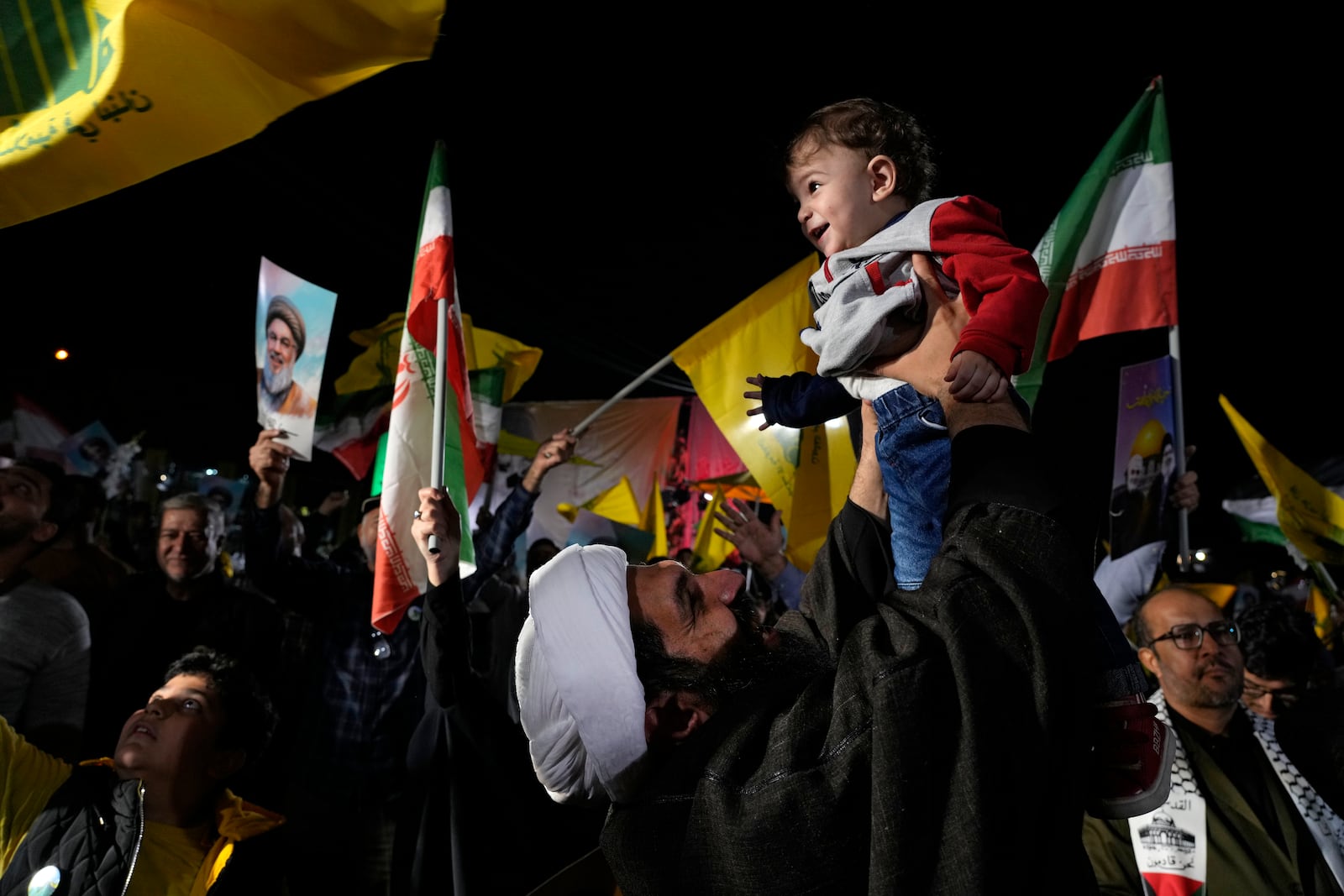 A cleric holds up his son as he celebrates Iran's missile strike against Israel during an anti-Israeli protest at Felestin (Palestine) Square in Tehran, Iran, Tuesday, Oct. 1, 2024. (AP Photo/Vahid Salemi)