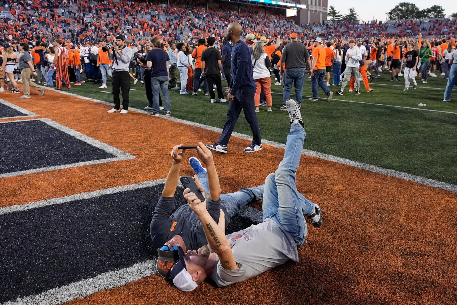 Two Illinois fans take selfies in the end zone after the team's 21-7 win over Michigan in an NCAA college football game Saturday, Oct. 19, 2024, in Champaign, Ill. (AP Photo/Charles Rex Arbogast)