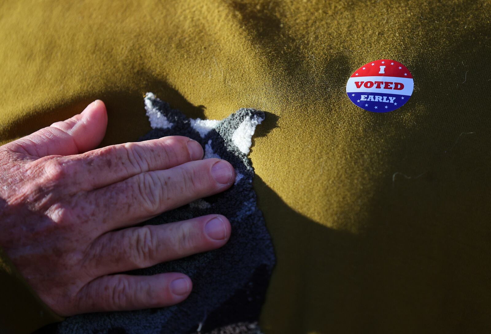 Minneapolis voter Scott Graham touches his heart while wearing an early voting sticker as he is interviewed at the City of Minneapolis early voting center, Friday, September 20, 2024, in Minneapolis, Minn. (AP Photo/Adam Bettcher)