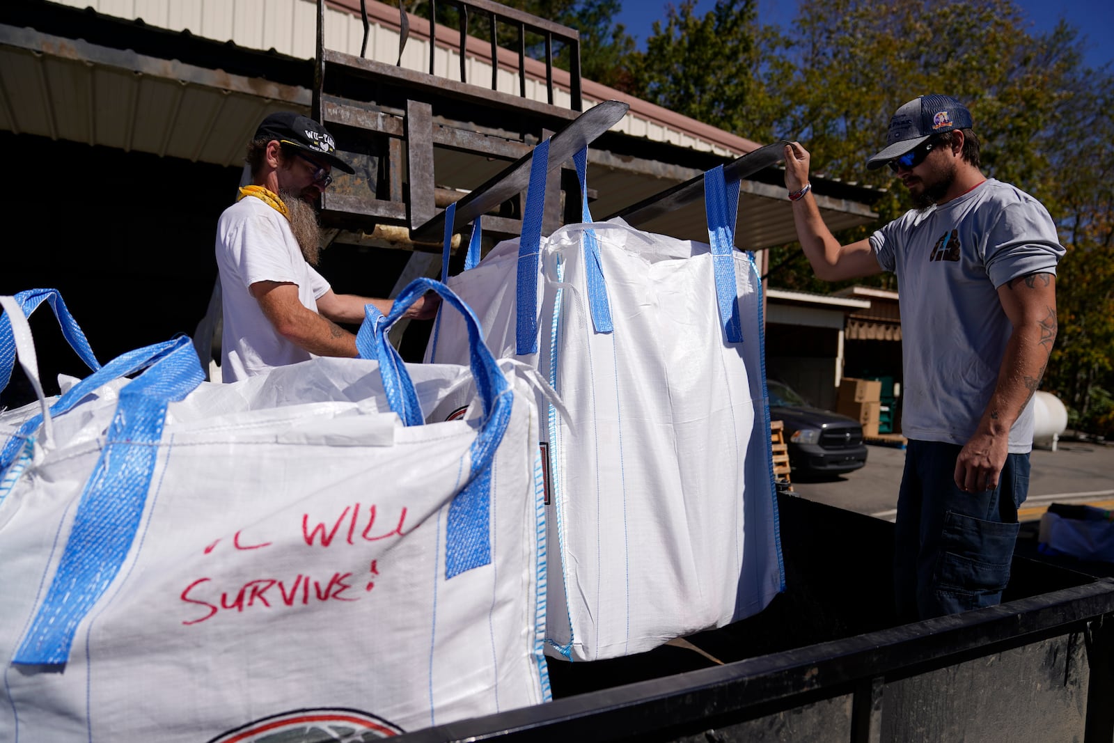 Volunteers "Boogie", left, and Andrew Buchholz, load food and supplies onto a truck at the Elk River Airport supply distribution center on Tuesday, Oct. 8, 2024, in Avery County, N.C. (AP Photo/Erik Verduzco)