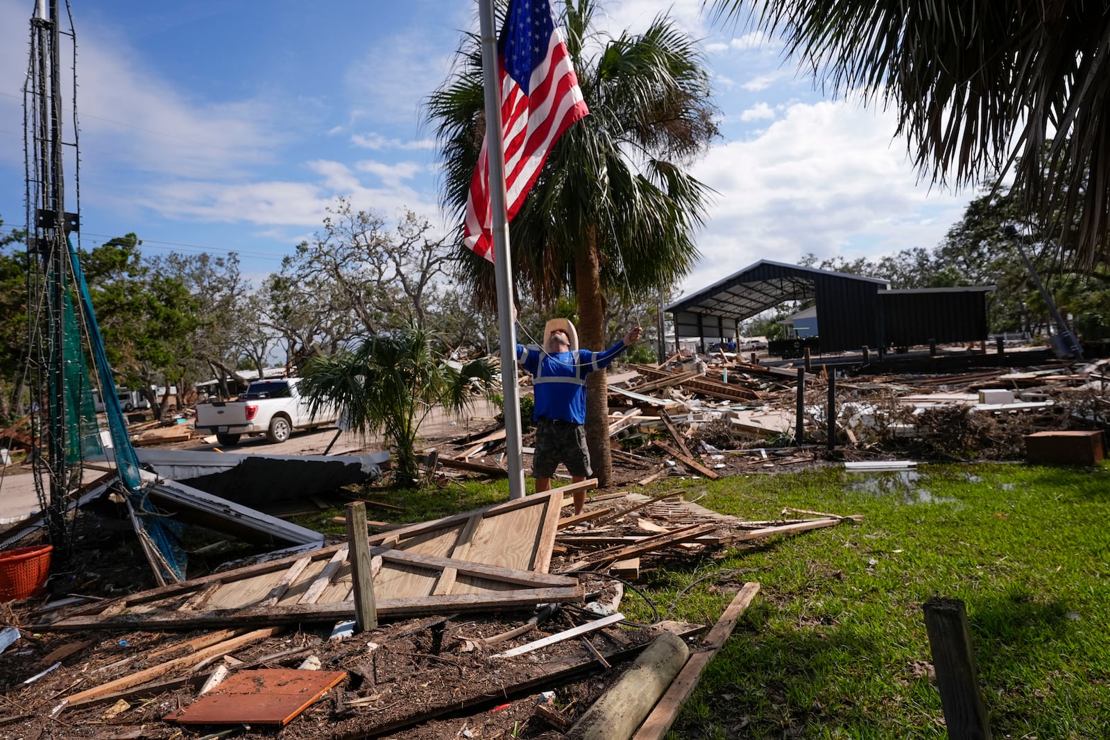 Chris Jordan, maintenance manager for Horseshoe Beach, hoists an American flag over the ruins of the city hall, in the aftermath of Hurricane Helene, in Horseshoe Beach, Fla., Saturday, Sept. 28, 2024. (AP Photo/Gerald Herbert)