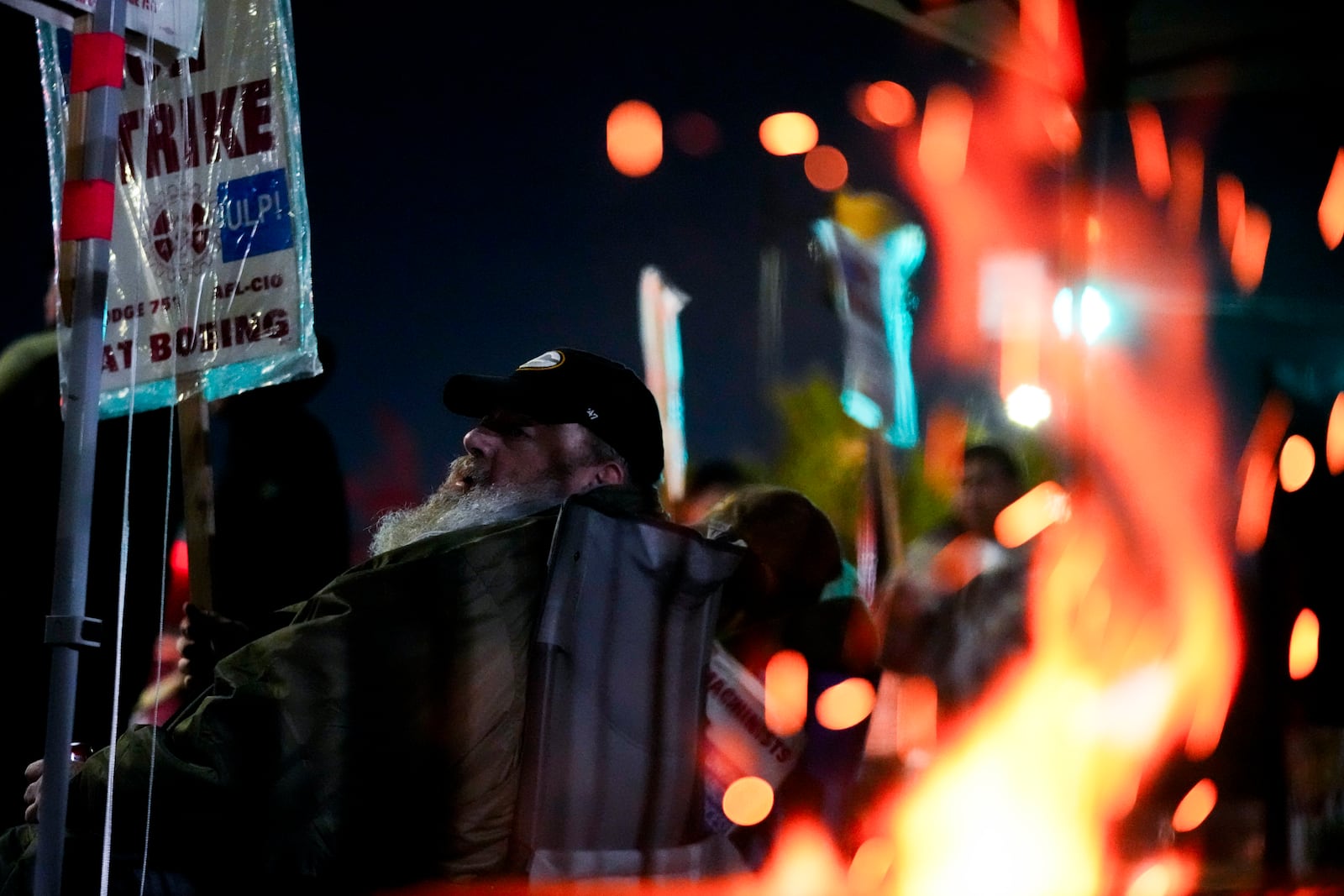 Bryan Osmundson, who has worked for Boeing for 24 years, sits with a picket sign near a burn barrel after union members voted to reject a new contract offer from the company, Wednesday, Oct. 23, 2024, in Renton, Wash. (AP Photo/Lindsey Wasson)