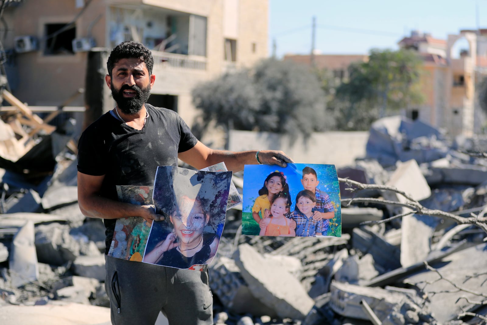 A man carries pictures of his relatives standing at the site of an Israeli airstrike in Saksakieh, south Lebanon, Thursday, Sept. 26, 2024. (AP Photo/Mohammed Zaatari)