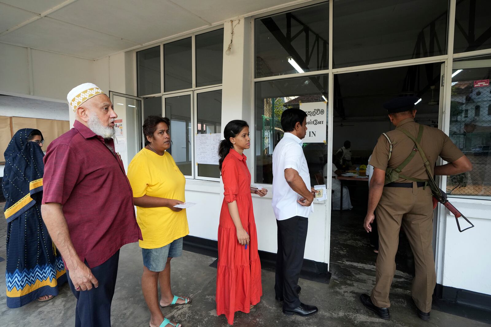 Sri Lankan police officer stands guard as voters queue to cast their vote at a polling center for presidential election in Colombo, Sri Lanka, Saturday, Sept. 21, 2024. (AP Photo/Rajesh Kumar Singh)