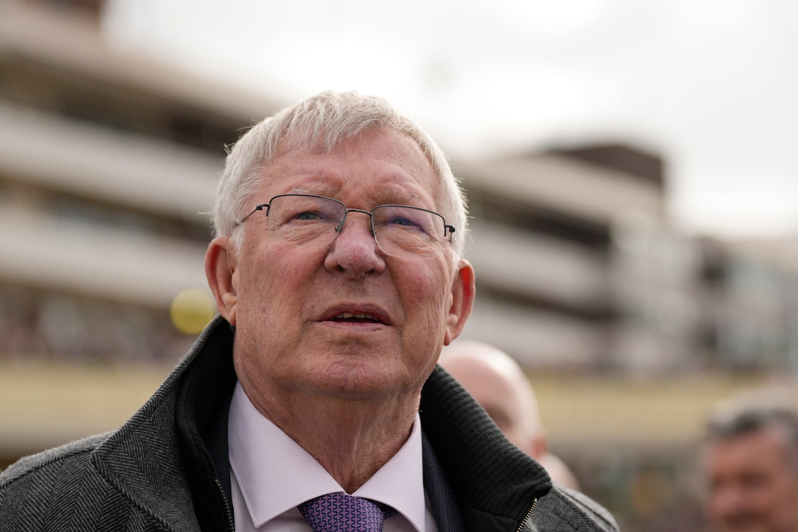 FILE - Former Manchester United manager Alex Ferguson, watches a large TV screen during The County Hurdle race as his horse L'Eau Du Sud came in second place behind Absurde, during the final day of the Cheltenham Festival at Cheltenham Racecourse, England, Friday, March 15, 2024. (AP Photo/Dave Shopland, File)