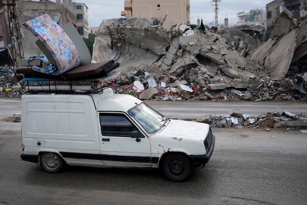 People in a car return back to their villages with their belongings after a ceasefire between Hezbollah and Israel began early morning, as they pass in front of a destroyed building that was hit in an Israeli airstrike, in Tyre, south Lebanon, Wednesday, Nov. 27, 2024. (AP Photo/Hussein Malla)