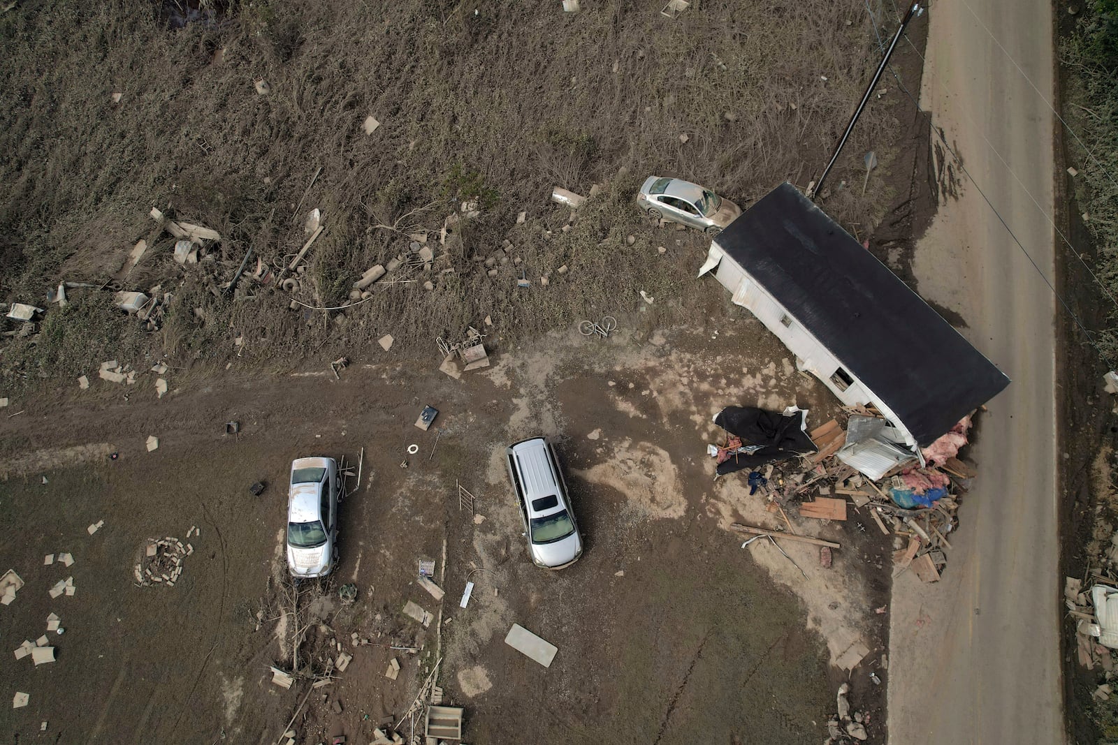 A destroyed mobile home and vehicles lay scattered across muddy land, Tuesday, Oct. 1, 2024, in Hendersonville, N.C., in the aftermath of Hurricane Helene. (AP Photo/Brittany Peterson)