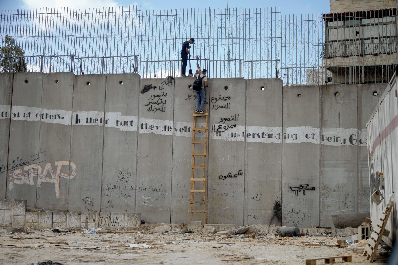 Palestinian men climb the separation wall at the town of al-Ram to illegally cross into Jerusalem, Sunday, Sept. 15, 2024. (AP Photo/Mahmoud Illean)