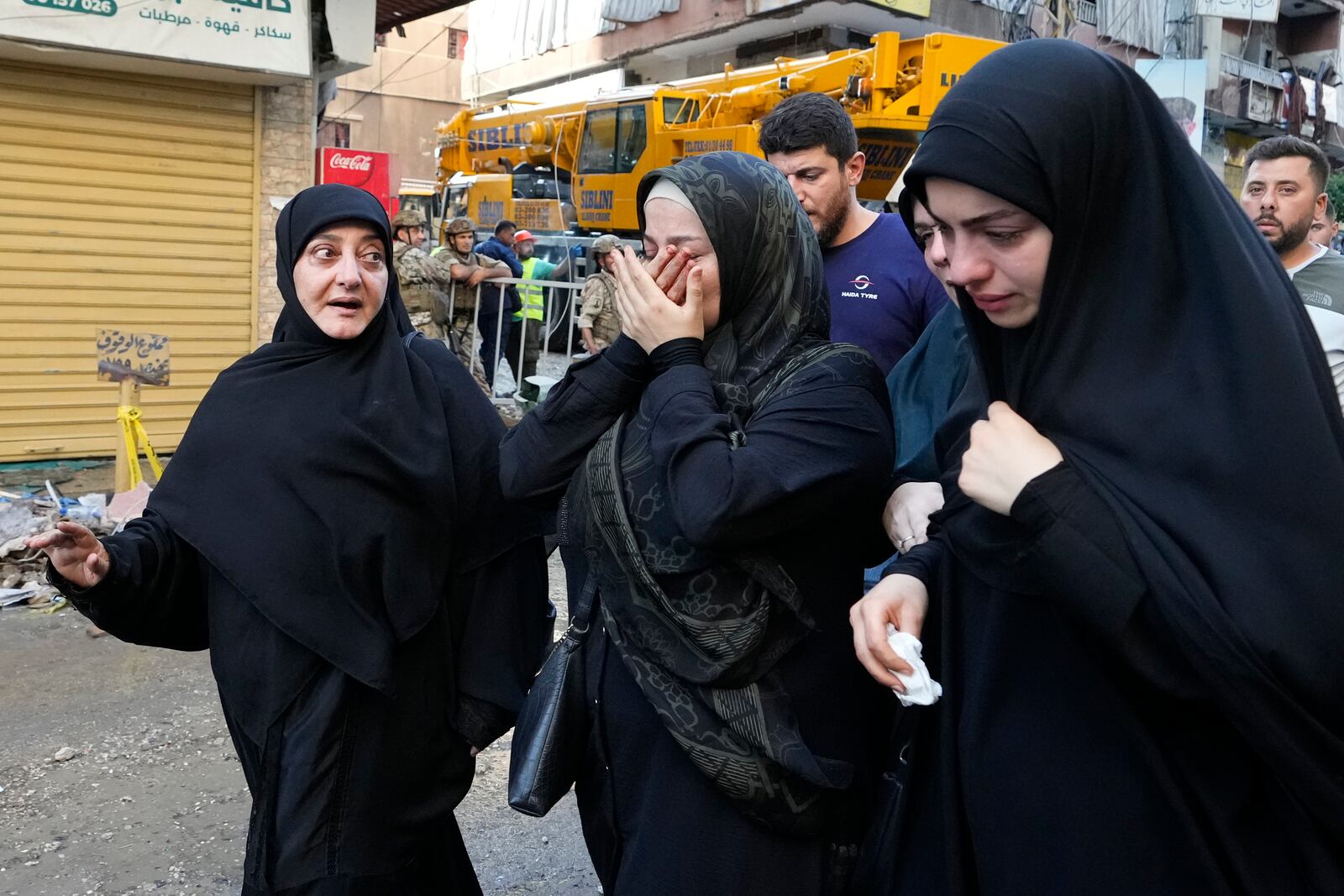 Residents cry as they walk past a building that was hit by an Israeli airstrike in Beirut's southern suburbs, Tuesday, Sept. 24, 2024. (AP Photo/Hassan Ammar)