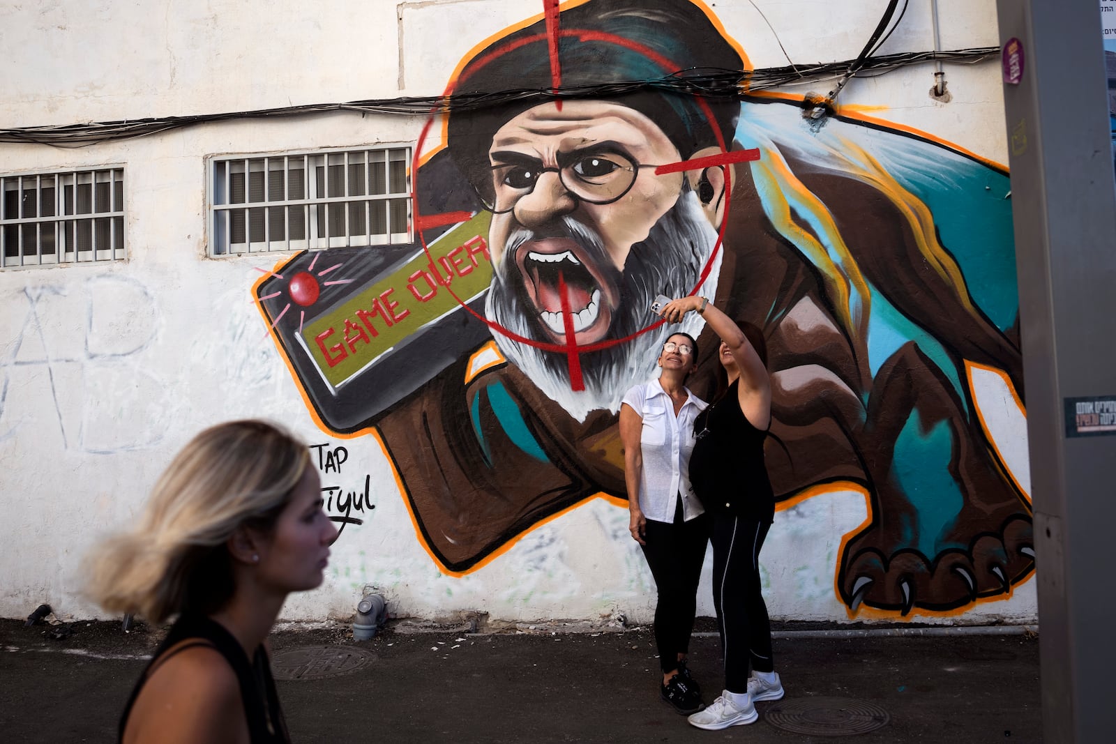 Two women take a selfie next to a newly painted graffiti of Hezbollah leader Hassan Nasrallah, a day after Hezbollah confirms its leader was killed in an Israeli airstrike, in Tel Aviv, Israel, on Sunday, Sept. 29, 2024. (AP Photo/Oded Balilty)