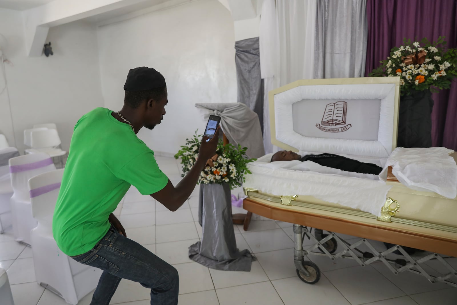 A morgue worker takes a photo of the body of Jean Louis Jeune Gracien, who was killed during an attack by armed gangs, at his funeral in Pont-Sonde, Haiti, Tuesday, Oct. 8, 2024. (AP Photo/Odelyn Joseph)