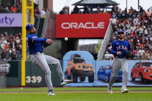 Texas Rangers pitcher Luke Jackson, left, throws to first base on a single hit by San Francisco Giants' Heliot Ramos during the ninth inning of a baseball game Sunday, April 27, 2025, in San Francisco. Ramos scored the winning run after throwing errors by Jackson and first baseman Jake Burger. (AP Photo/Godofredo A. Vásquez)