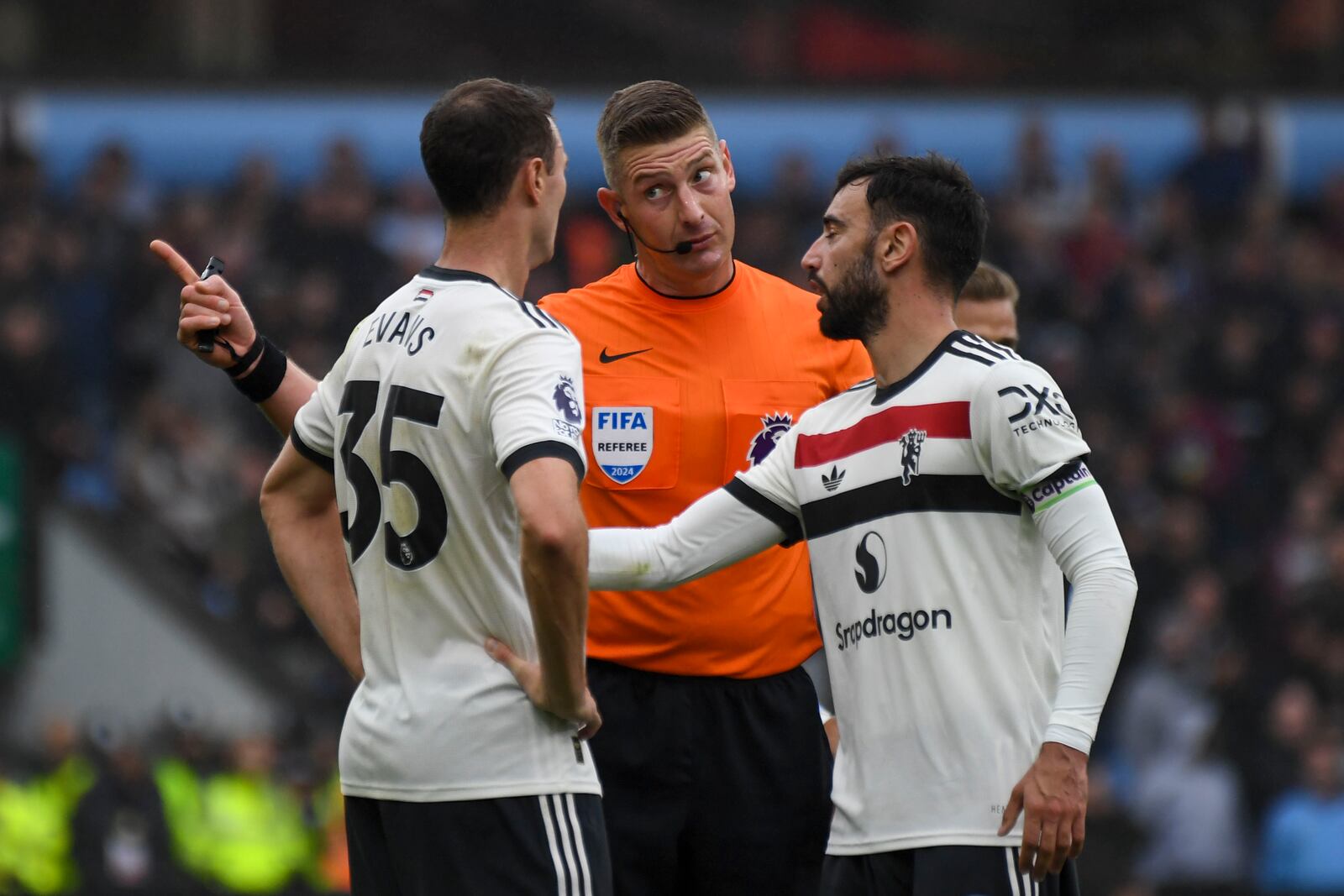 Referee Robert Jones, center, speaks with Manchester United's Jonny Evans, left, and Manchester United's Bruno Fernandes during the English Premier League soccer match between Aston Villa and Manchester United, at Villa Park in Birmingham, England, Sunday, Oct. 6, 2024. (AP Photo/Rui Vieira)