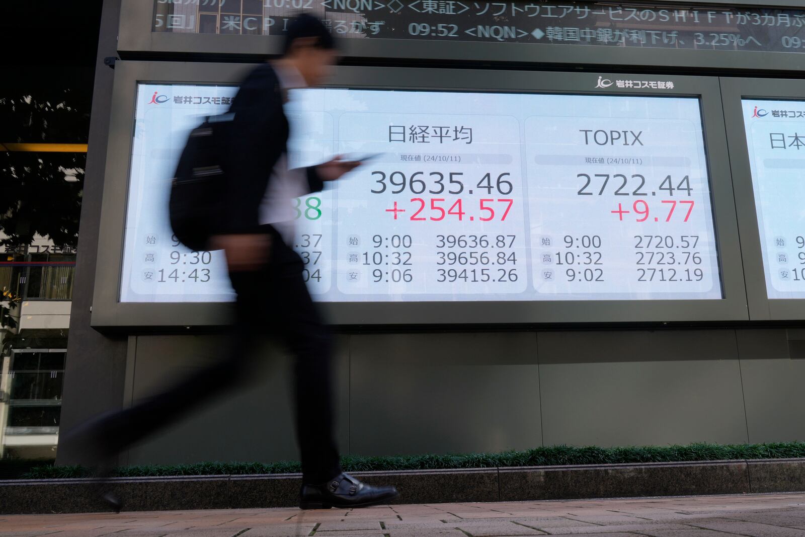 A passerby walks past an electronic stock board showing Japan's Nikkei 225 index, center, in front of a securities building Friday, Oct. 11, 2024 in Tokyo. (AP Photo/Shuji Kajiyama)