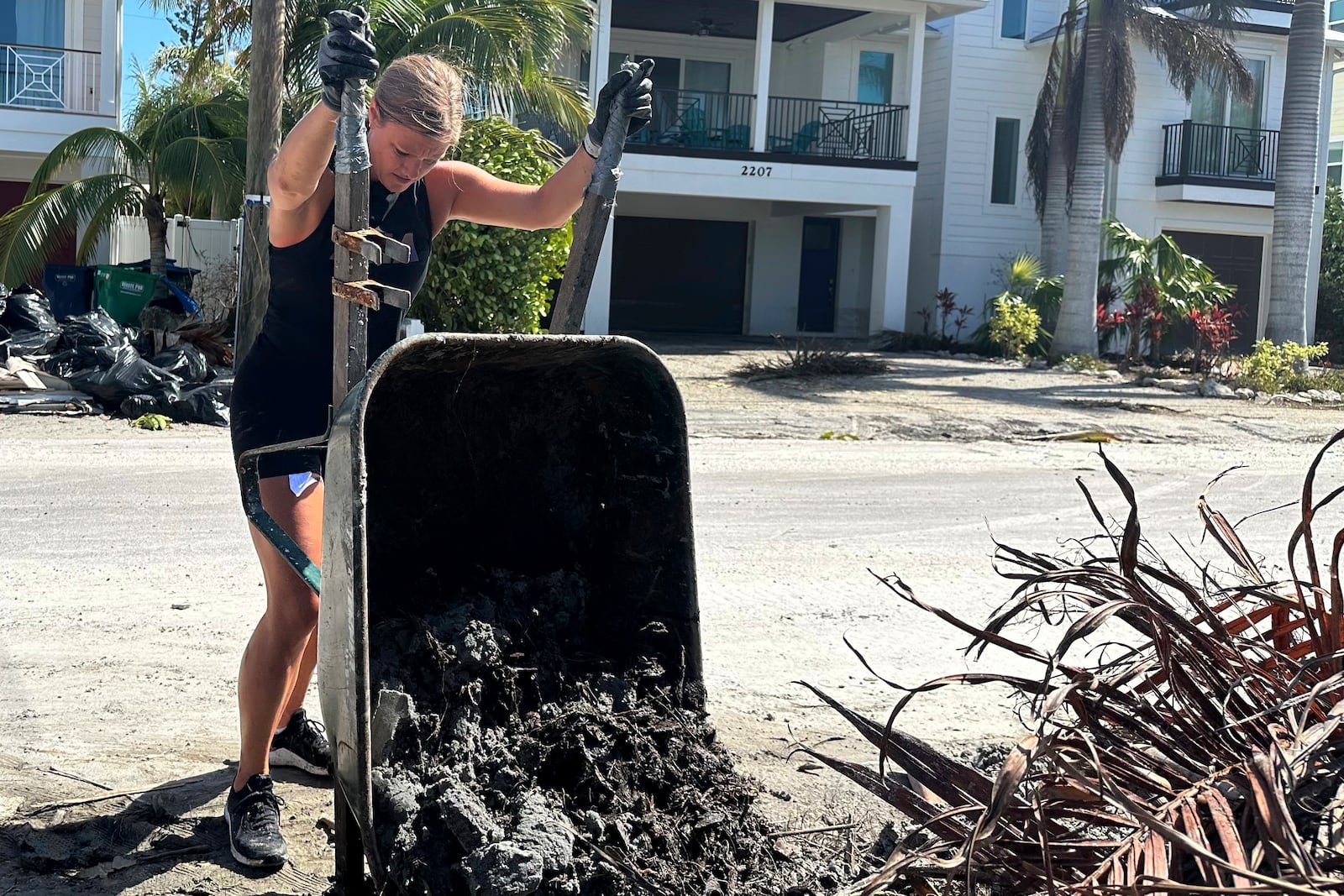 Jen Hilliard dumps sandy muck from a wheelbarrow in the aftermath of Hurricane Milton on Saturday, Oct. 12, 2024, outside a friend’s house in Bradenton Beach, Fla. (AP Photo/Russ Bynum)