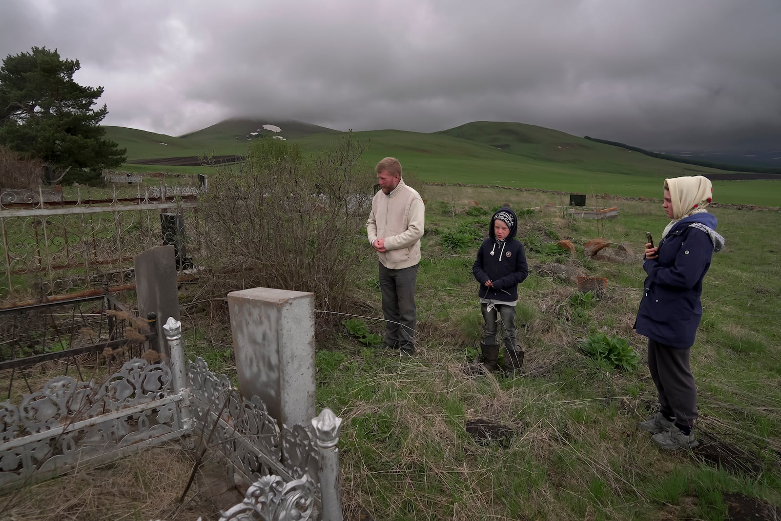 Yuri Strukov, 46, his son Ilya, 10, and his daughter Daria, 21, pray at the Doukhobor cemetery outside of the remote mountain village of Orlovka, Georgia, Saturday, May 4, 2024. (AP Photo/Kostya Manenkov)