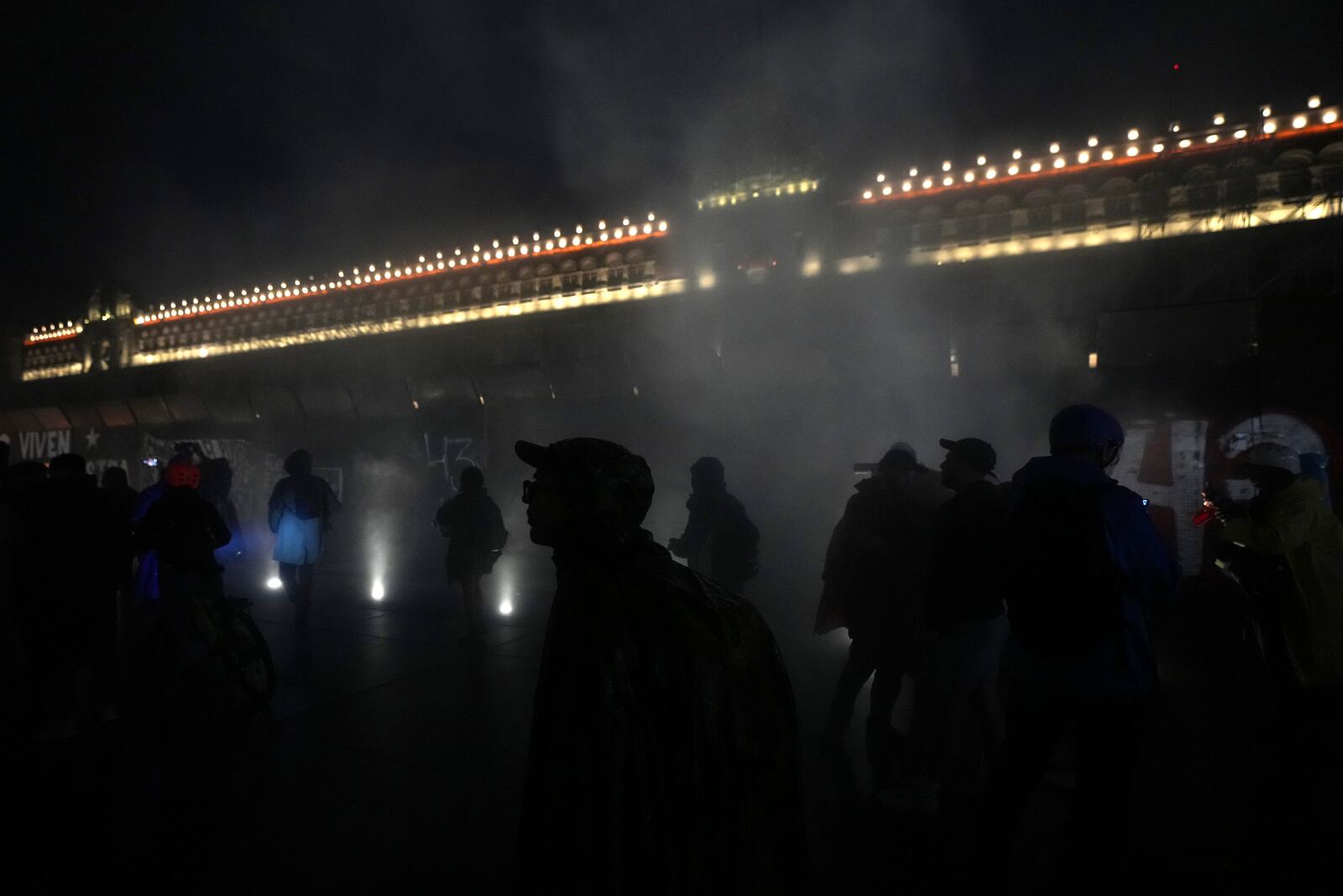 Youths are silhouetted in clouds of smoke caused by fire balls thrown at the barriers protecting the facade of the National Palace during a demonstration marking the 10-year anniversary of the disappearance of 43 students from an Ayotzinapa rural teacher's college, in Mexico City, Thursday, Sept. 26, 2024. (AP Photo/Fernando Llano)