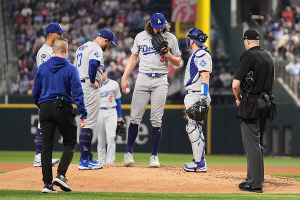 Los Angeles Dodgers infielders, umpire Nic Lentz, right, and a team staff member check on starting pitcher Tyler Glasnow, who left the game with an unknown injury, in the fifth inning of a baseball game against the Texas Rangers in Arlington, Texas, Sunday, April 20, 2025. (AP Photo/Tony Gutierrez)