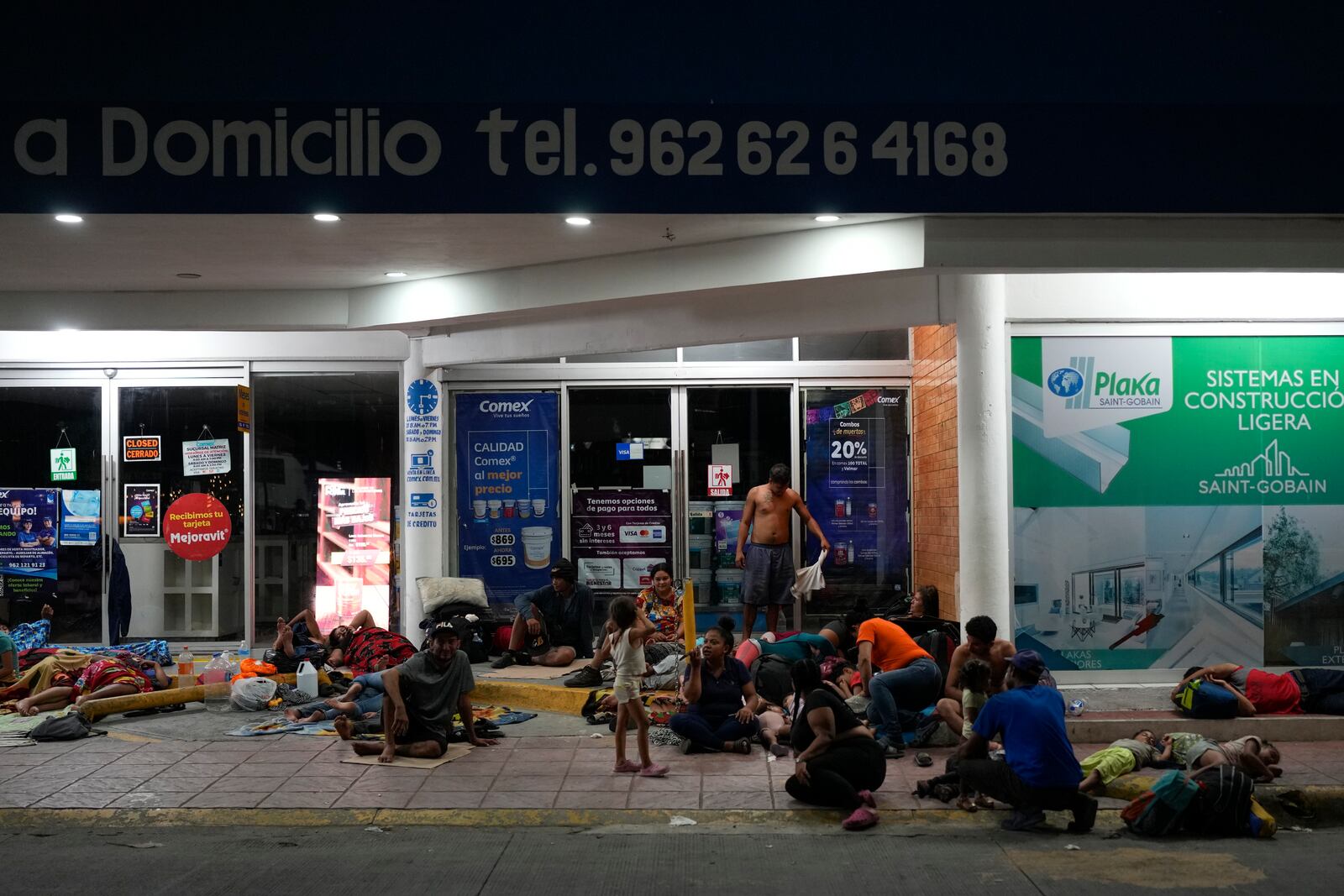 Migrants rest in front of a paint shop in Tapachula, Mexico, Sunday, Oct. 27, 2024. (AP Photo/Matias Delacroix)