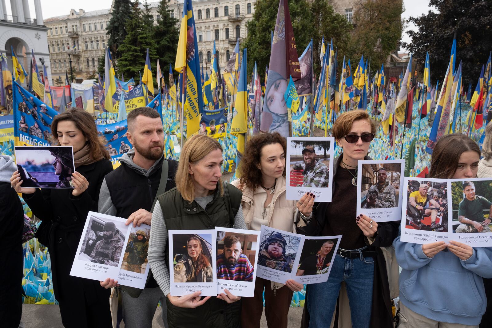 People hold photos of their relatives soldiers to keep a nationwide minute of silence in memory of fallen soldiers, who defended their homeland in war with Russia, on Defenders Day at the improvised war memorial in Independence square in Kyiv, Ukraine, Tuesday, Oct. 1, 2024. (AP Photo/Efrem Lukatsky)