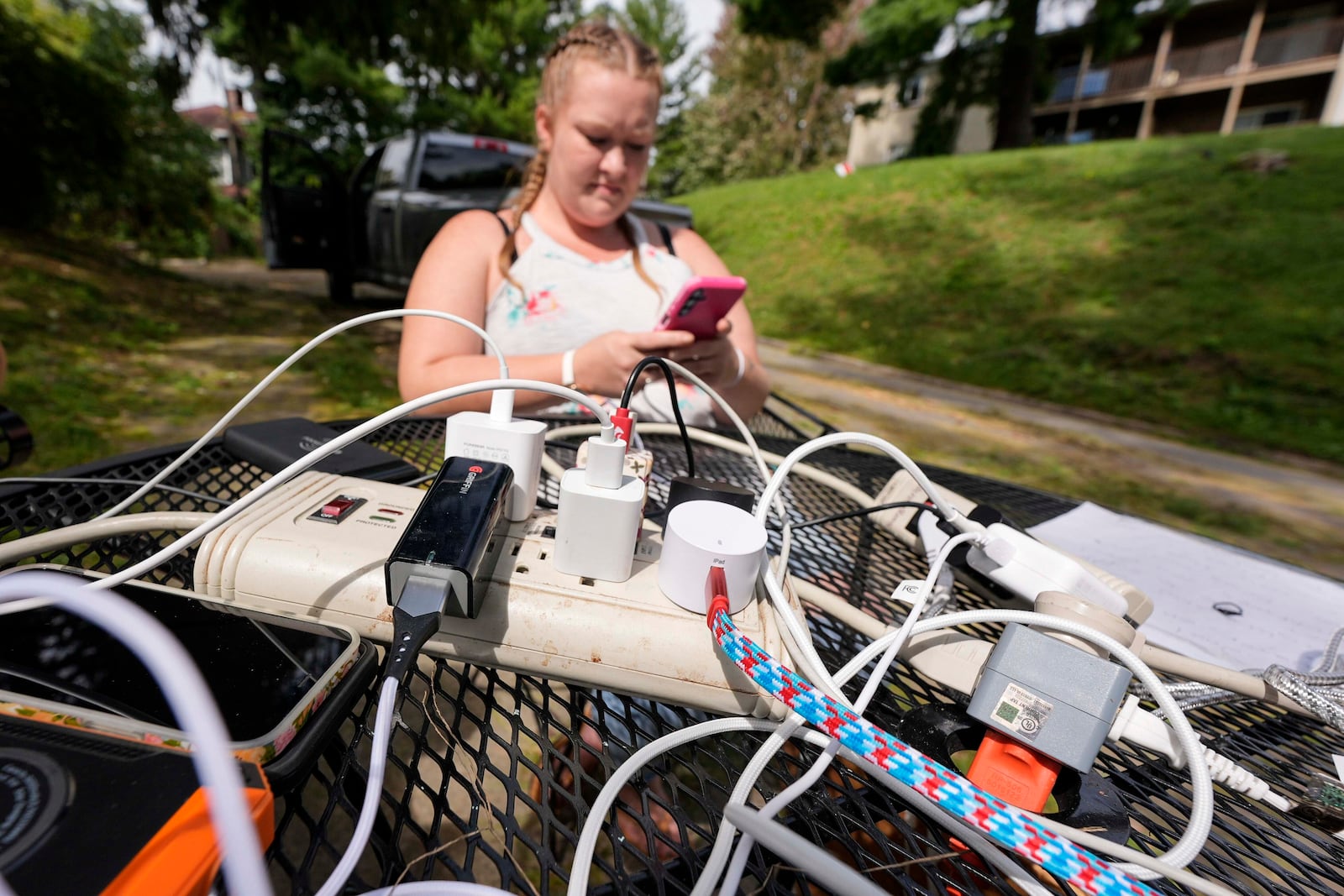 Carrie Owenby looks at her phone as a neighbor with power dropped an extension cord for neighbors who have no power in the aftermath of Hurricane Helene, Monday, Sept. 30, 2024, in Ashville, N.C. (AP Photo/Mike Stewart)