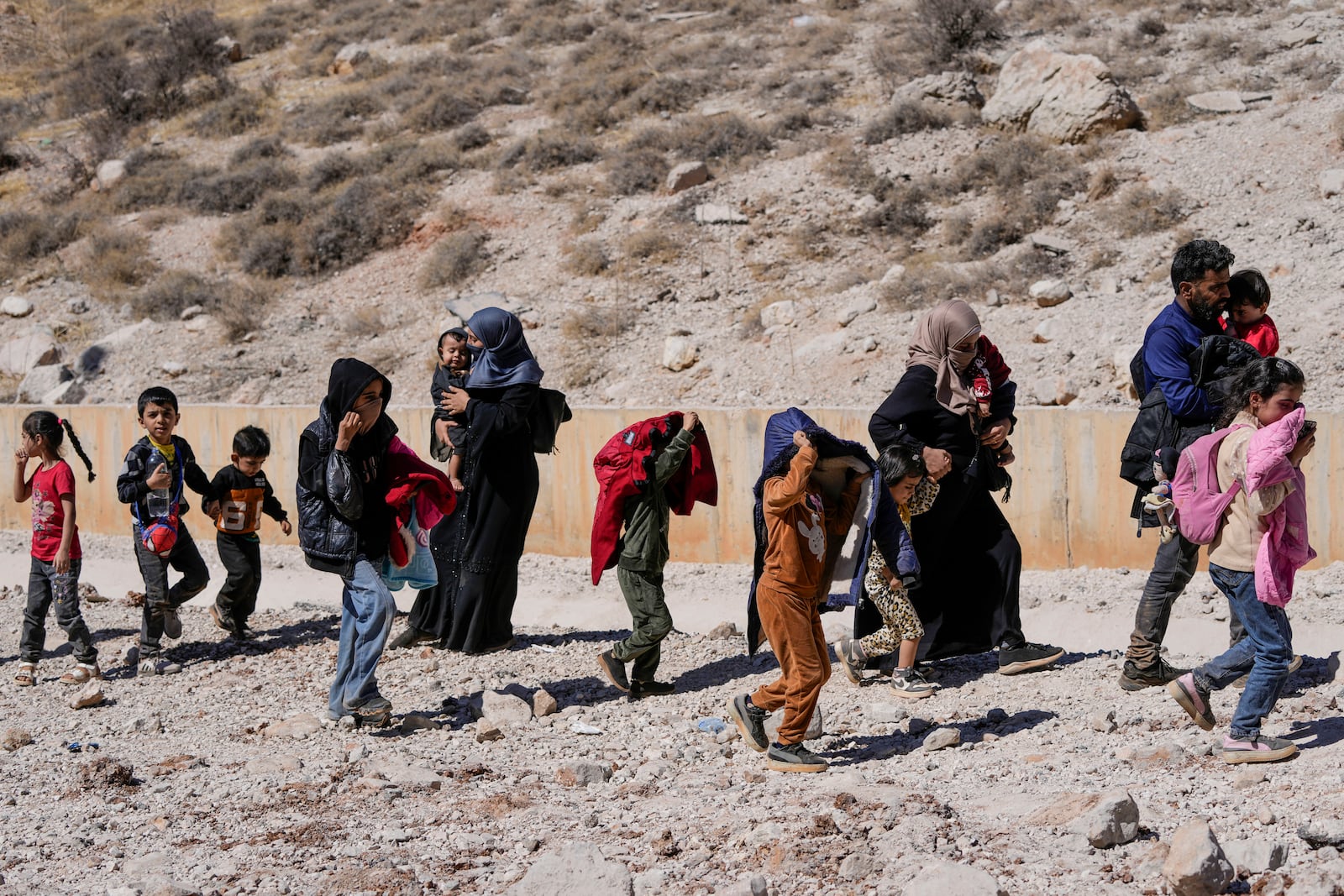 Families cross into Syria on foot, through a crater caused by Israeli airstrikes aiming to block Beirut-Damascus highway at the Masnaa crossing, in the eastern Bekaa Valley, Lebanon, Saturday, Oct. 5, 2024. (AP Photo/Hassan Ammar)