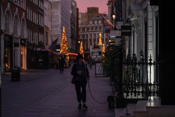 A woman walks a dog in a street of Mayfair at sunrise, in London, Friday, Nov. 29, 2024.(AP Photo/Alberto Pezzali)