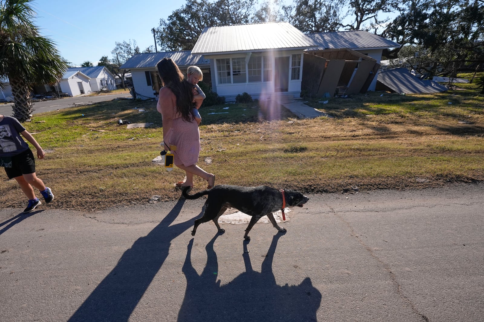 A loose dog walks past a group from St. Augustine, Fla., who did not want to give their name, that arrived to help storm victims, as they walk to pray outside the damaged First Baptist Church in the aftermath of Hurricane Helene, in Horseshoe Beach, Fla., Sunday, Sept. 29, 2024. (AP Photo/Gerald Herbert)