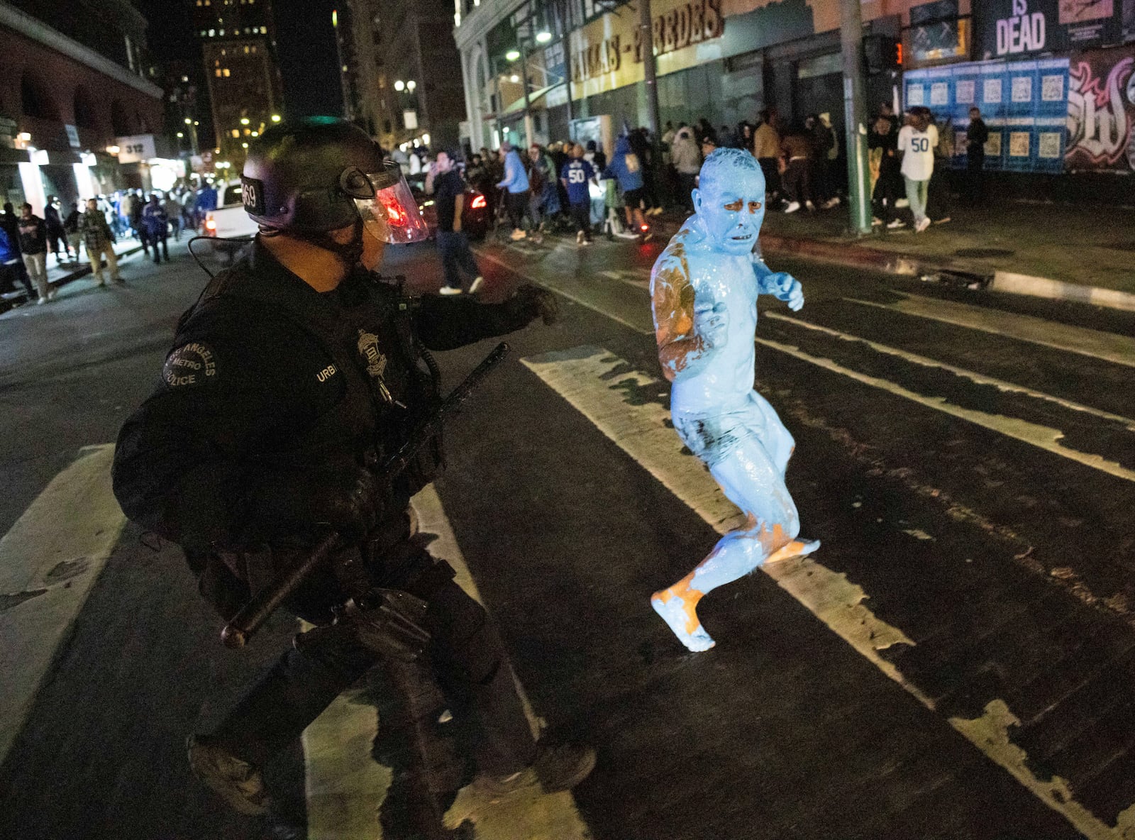 A person covered in blue paint runs from a police officer as fans celebrate on streets after the Los Angeles Dodgers won against the New York Yankees in the baseball World Series Wednesday, Oct. 30, 2024, in Los Angeles. (AP Photo/Ethan Swope)