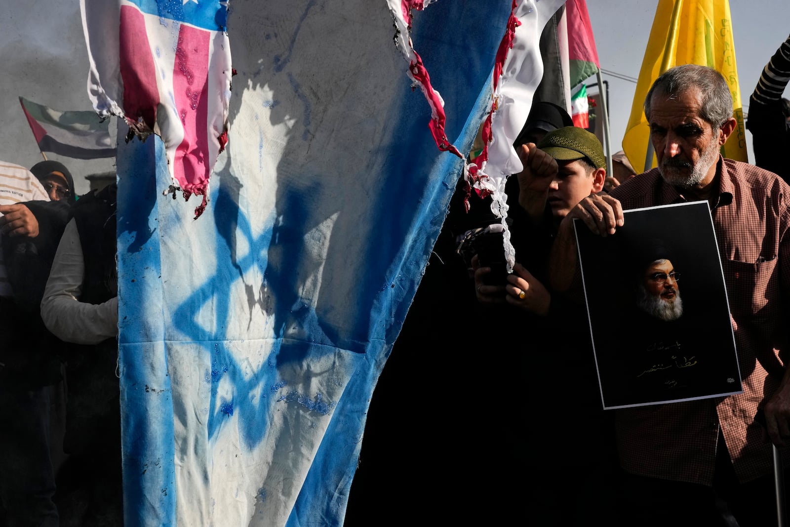 Representations of the U.S. and Israeli flags are set on fire as a demonstrator holds a poster of slain Hezbollah leader Hassan Nasrallah in a rally commemorating him, in Tehran, Iran, Wednesday, Oct. 2, 2024. (AP Photo/Vahid Salemi)