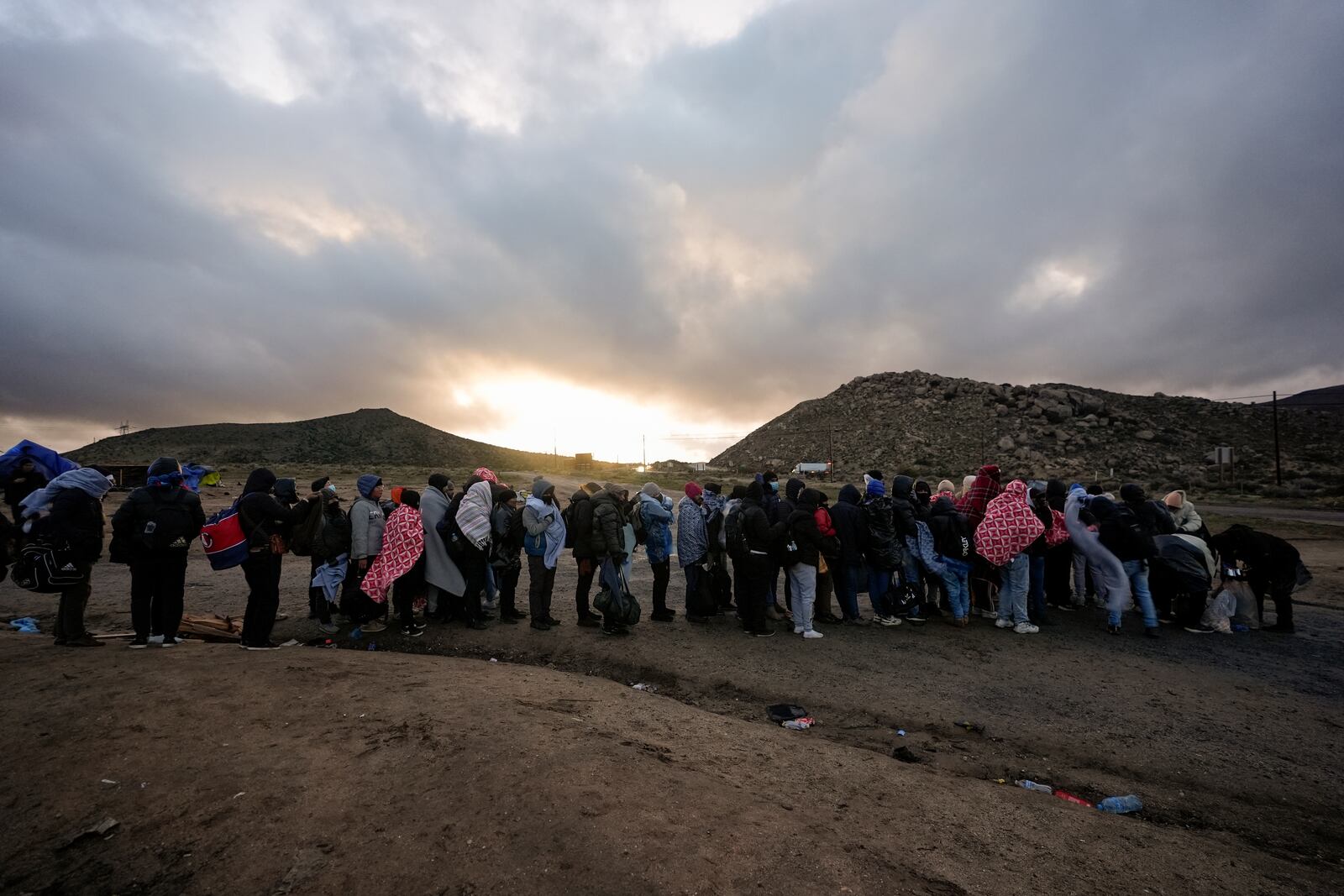 FILE - Asylum-seeking migrants line up in a makeshift, mountainous campsite to be processed after crossing the border with Mexico, Friday, Feb. 2, 2024, near Jacumba Hot Springs, Calif. (AP Photo/Gregory Bull, File)