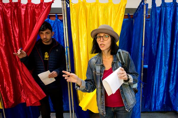 People exit voting cabins with the colours of the Romanian flag as curtains, before casting their vote, in the second round of the country's presidential election redo in Bucharest, Romania, Sunday, May 18, 2025. (AP Photo/Andreea Alexandru)