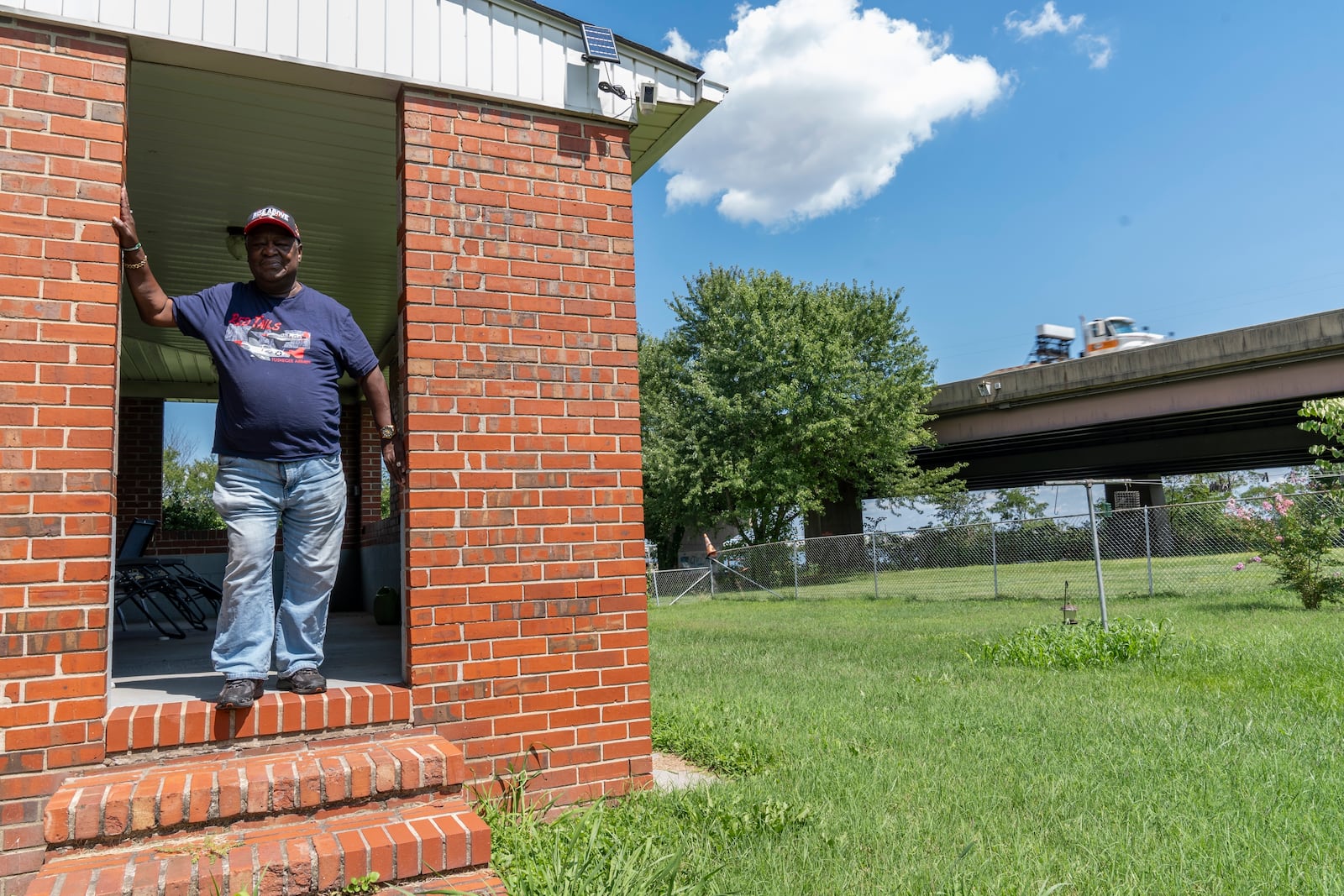 Linwood Jackson poses for a portrait outside of his home, Tuesday, Aug. 13, 2024, as a semi truck drives past on the remaining portion of the Francis Scott Key Bridge in Turner Station, Md. (AP Photo/Stephanie Scarbrough)